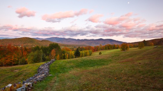 A stone wall in a hay field in Sugar Hill, New Hampshire. The Franconia Range in the White Mountains is in the distance. Sunset.