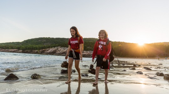 Two teenagers walk barefoot on Sand Beach after a hike in Maine's Acadia National Park.